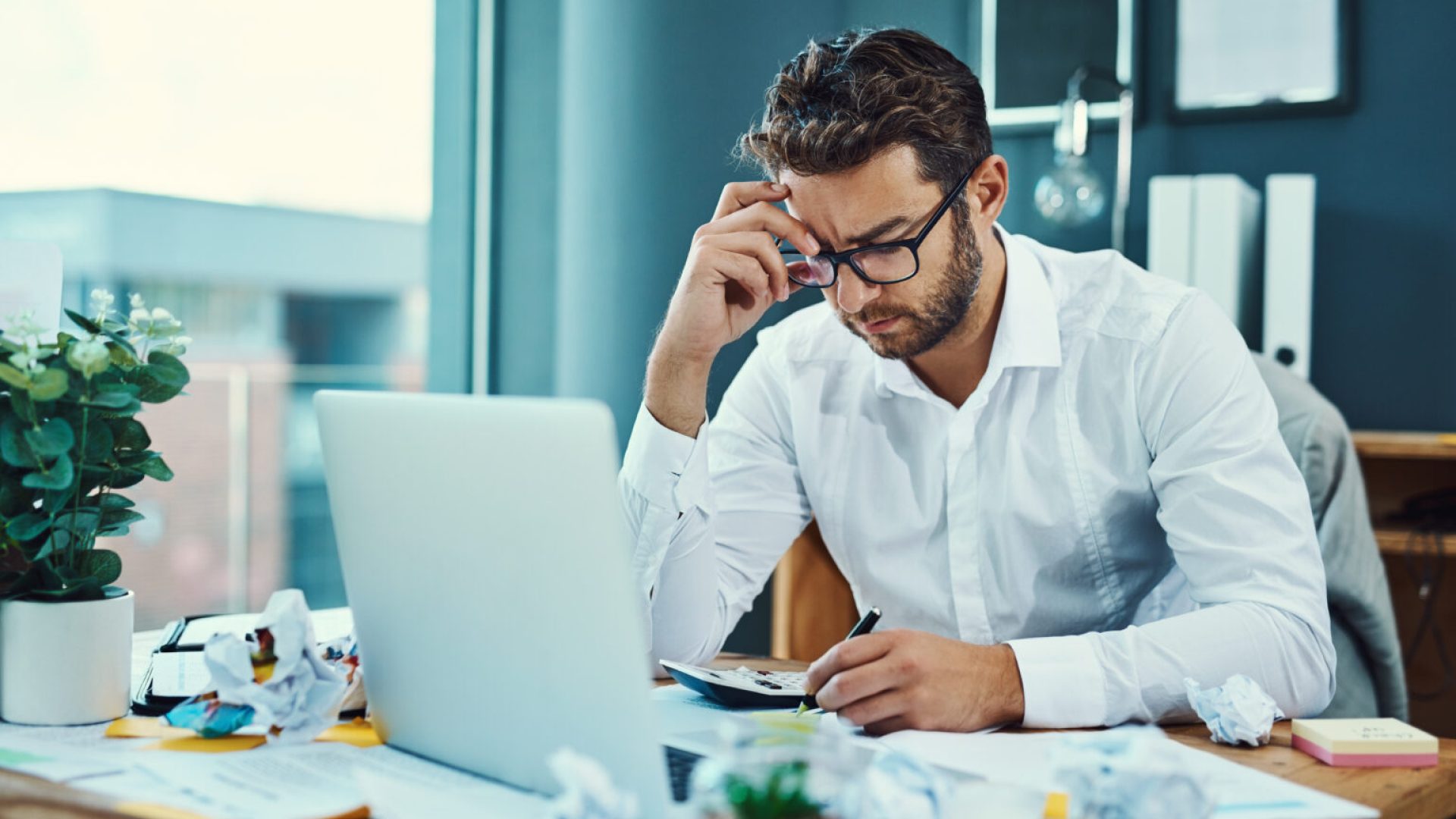 Shot of a young businessman looking stressed out while working on a laptop in an office.